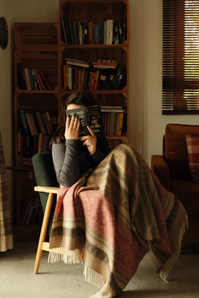 An adult peacefully using a weighted lap pad while reading a book in a cozy nook.