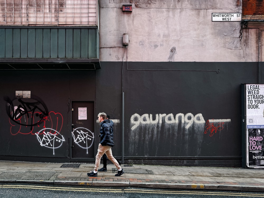 a woman walking down a street past a wall covered in graffiti