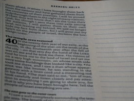 A close-up image of an open Bible page showing text from the book of Ezekiel, specifically chapter 40:11. The text is formatted in two columns with a section title in bold reading 'The temple area restored'. The paper is off-white, and the printing is in black ink.