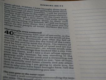 A close-up image of an open Bible page showing text from the book of Ezekiel, specifically chapter 40:11. The text is formatted in two columns with a section title in bold reading 'The temple area restored'. The paper is off-white, and the printing is in black ink.