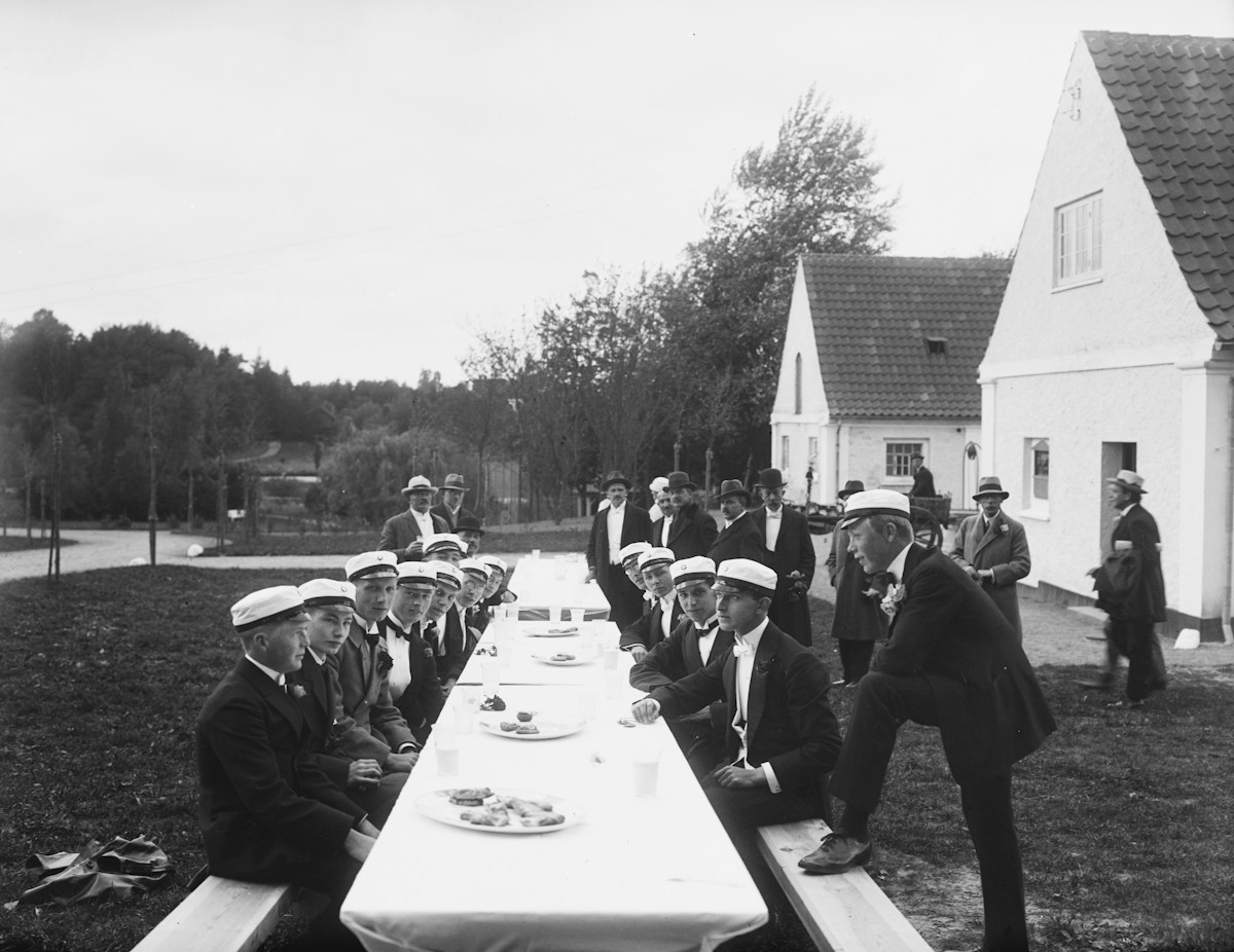 A group of young men sitting at a long table, discussing high school graduation party ideas and planning.