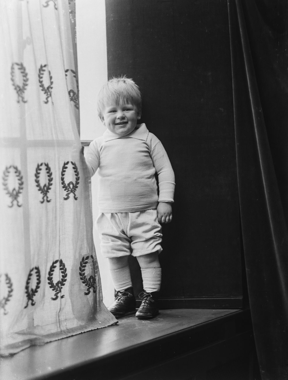 a little boy that is standing in front of a curtain