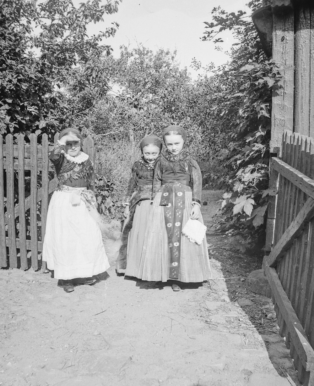 a black and white photo of three women standing in front of a fence