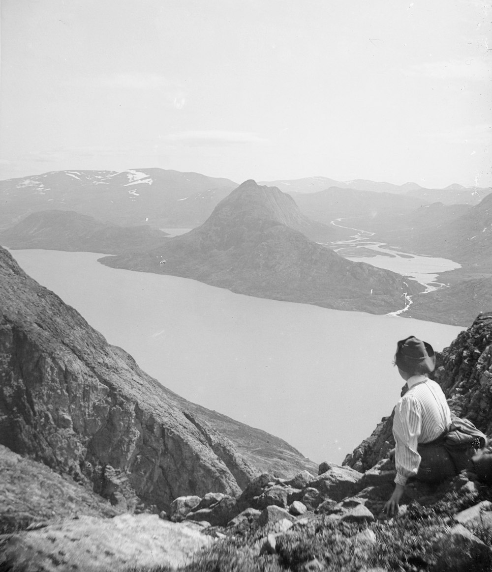 a man sitting on top of a mountain next to a lake