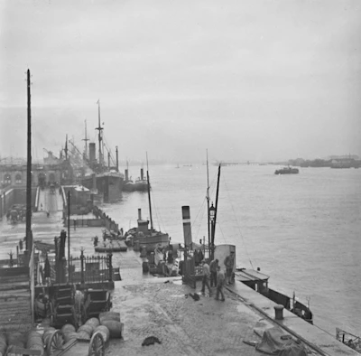 Black and white photo of the ship docked in a busy harbor from the early 1900s.