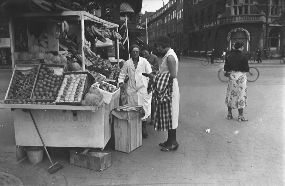 a black and white photo of people at a fruit stand