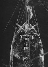 A bird's-eye view of a boat filled with various supplies and equipment, including coiled ropes, fabric, and possibly containers. The deck is cluttered, suggesting preparation or aftermath of a sea voyage. Rigging and a mast extend vertically from the center of the boat.