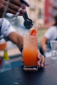 a person pouring a drink into a tall glass