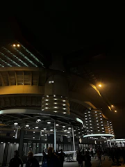 Wide shot of the Emilio Roto stadium lit up at night with fans entering.