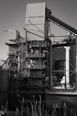 A large industrial structure with multiple interconnected metal pipes and storage units, featuring angular and cylindrical shapes. The image depicts a complex assembly of platforms, ladders, and scaffolding arranged around rectangular and cylindrical components.