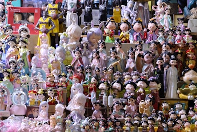 A collection of various figurines and dolls, including traditional Chinese-style characters and modern designs, is displayed on shelves. The figurines are dressed in colorful, ornate costumes, and some characters represent basketball players in jerseys. The scene is vibrant and slightly chaotic due to the vast array of items on display.