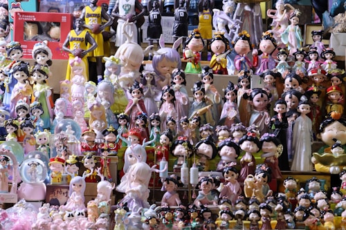 A collection of various figurines and dolls, including traditional Chinese-style characters and modern designs, is displayed on shelves. The figurines are dressed in colorful, ornate costumes, and some characters represent basketball players in jerseys. The scene is vibrant and slightly chaotic due to the vast array of items on display.