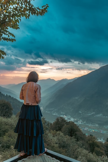 A smiling traveler standing on a scenic mountain overlook at sunset.