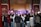 A large crowd gathers indoors facing a performance stage. The stage features traditional musical instruments like drums and bell chimes, and performers dressed in cultural attire. The audience captures the moment on their phones amidst ornate wall decorations and wooden architectural details.