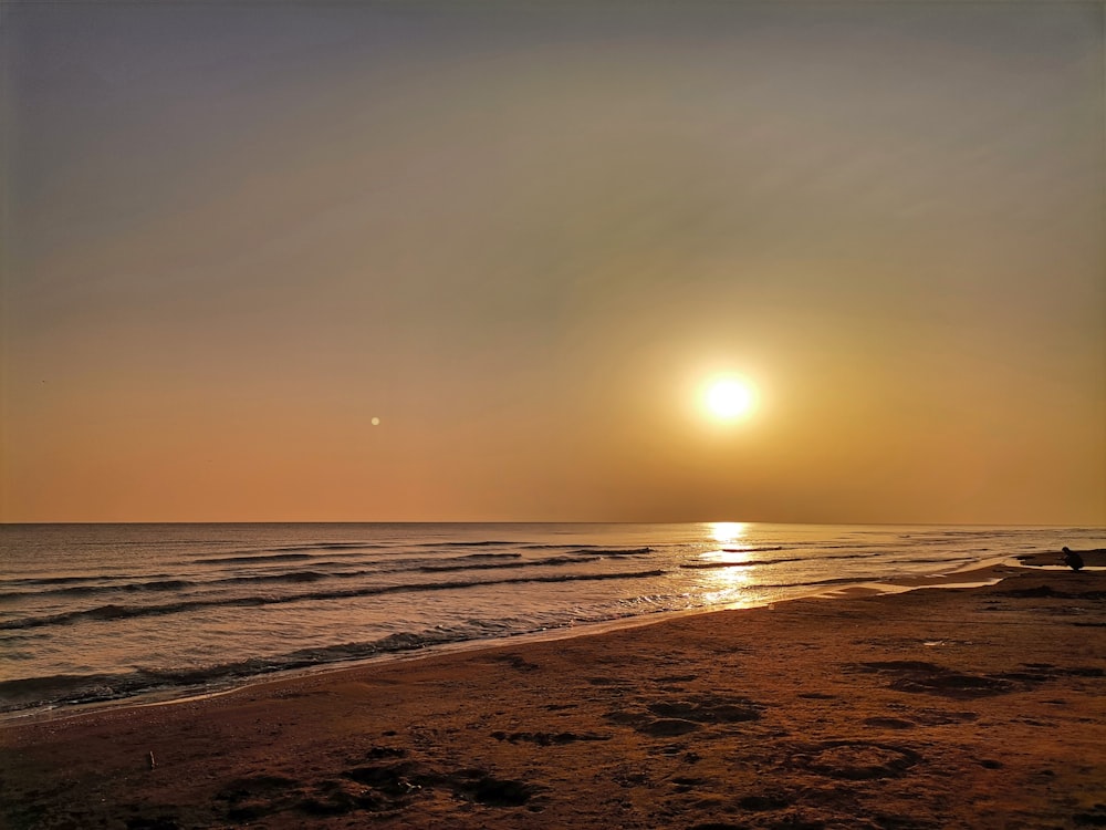 the sun is setting over the ocean on the beach