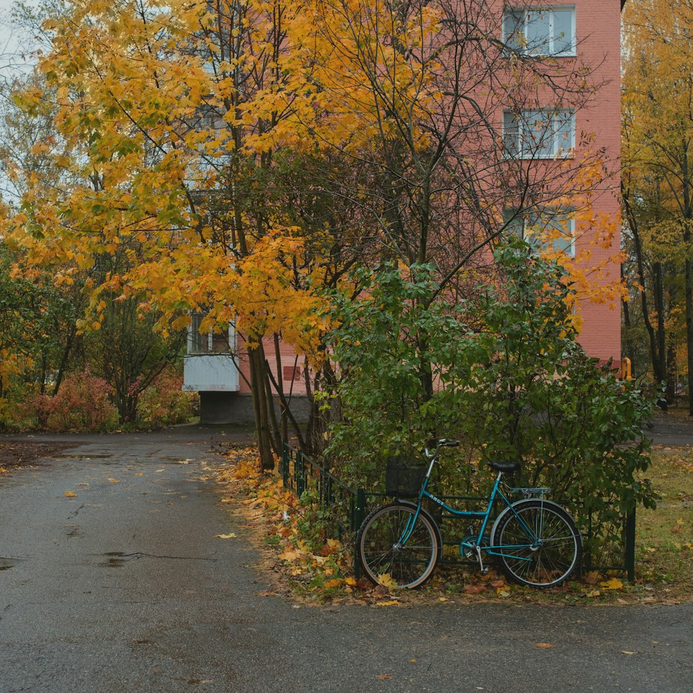 una bicicleta azul estacionada junto a un árbol con hojas amarillas