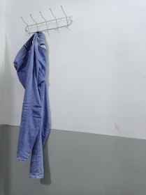 A pair of sleek dark blue jeans hanging from a modern metal rack with a soft blue wall behind.