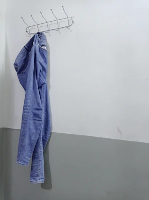 Artistic shot of denim jeans hanging on a minimalist rack against a white wall.