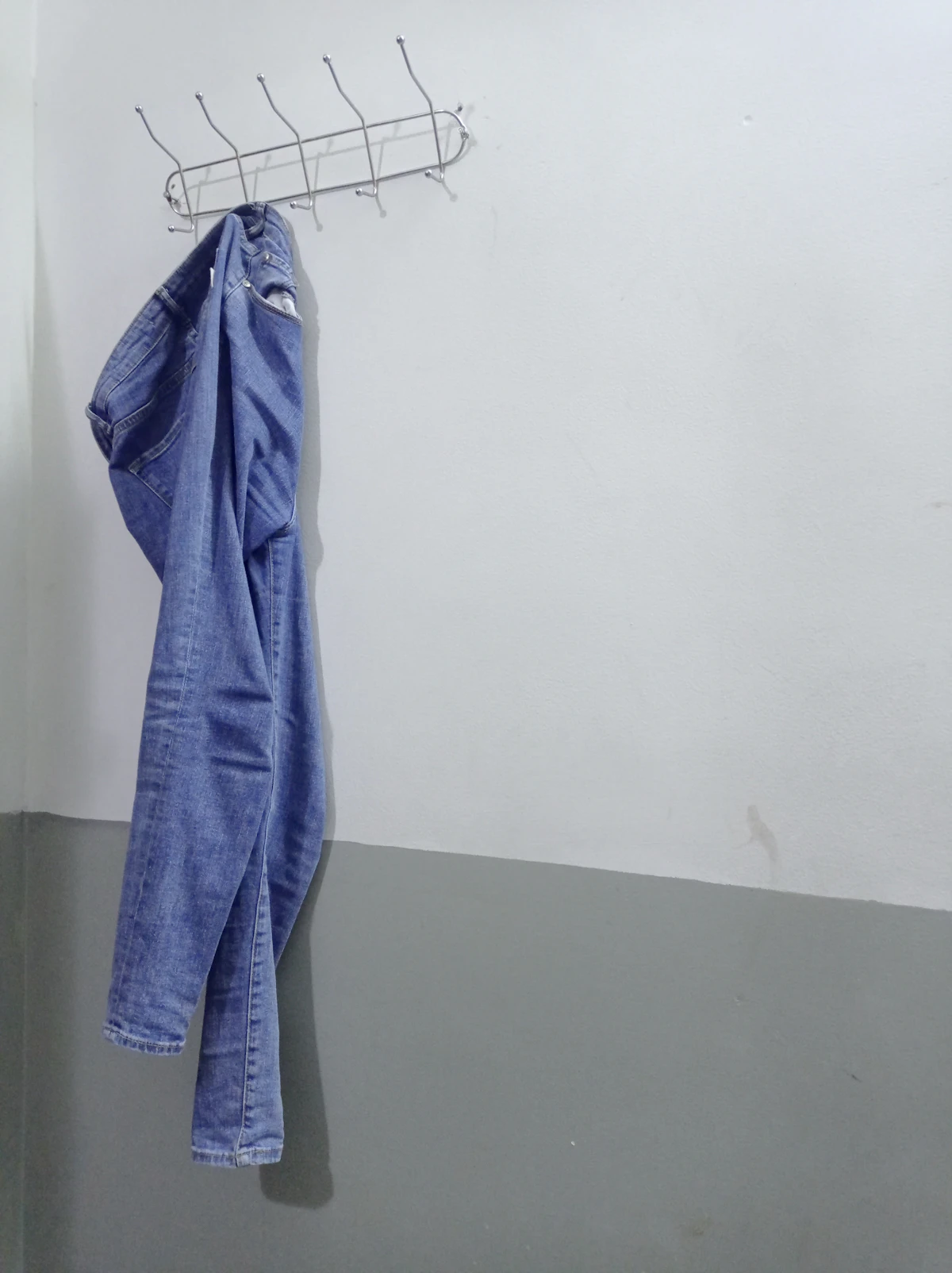 Light blue denim jacket hanging on wooden hanger against white wall