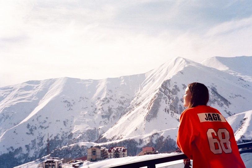 a woman in a red jacket looking at a snowy mountain