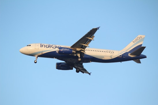 A commercial airplane in flight against a clear blue sky, with landing gear extended and the name of the airline visible on its side.