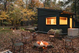 Modern black cabin in an autumn forest with a glowing firepit