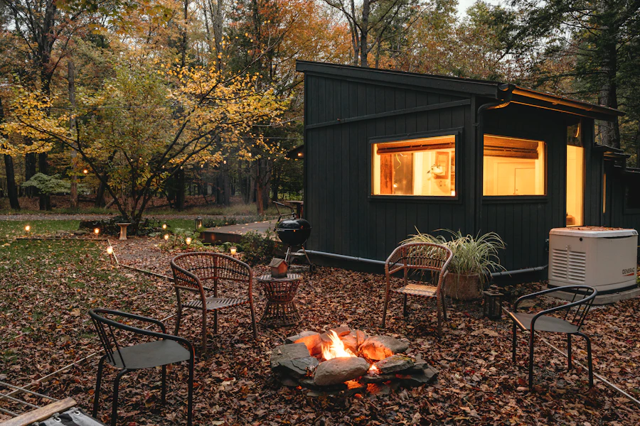 Modern black cabin in an autumn forest with a glowing firepit