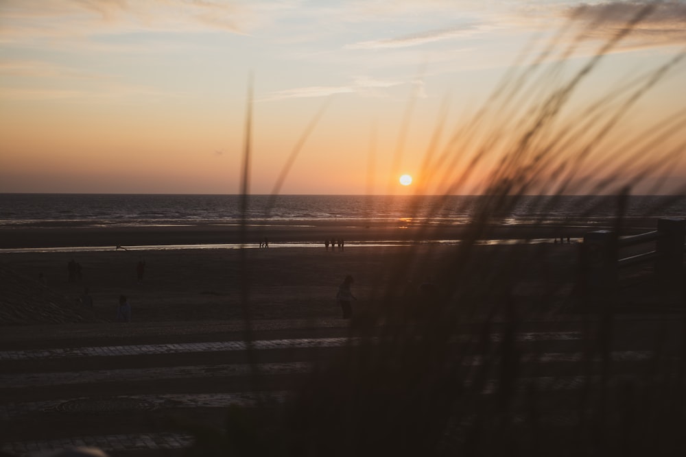 the sun is setting over the beach with people walking