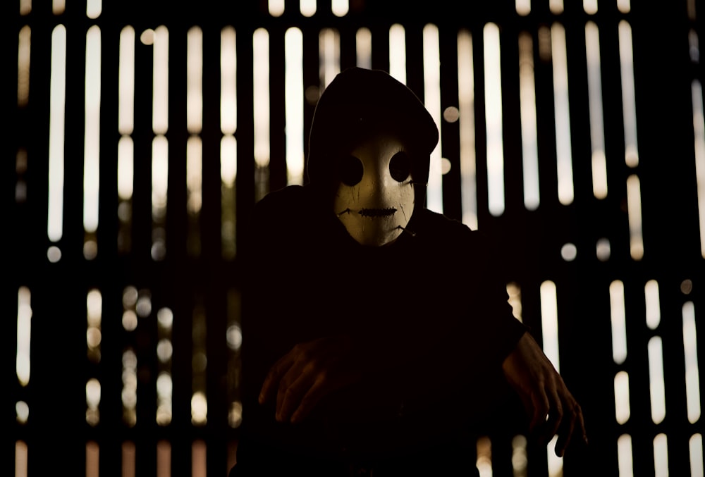 a person wearing a mask in front of a fence