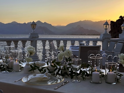 A beautifully set outdoor table with golden accents, overlooking a peaceful green valley at sunset.