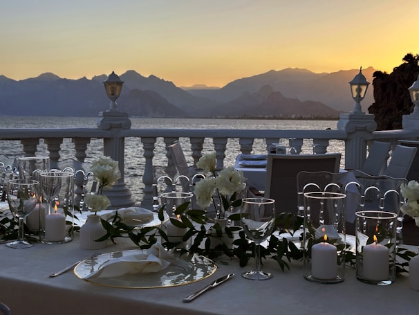 A panoramic view of a luxurious dining setup overlooking a serene Indian landscape at sunset.