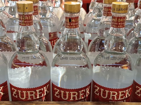 Several glass bottles with yellow caps are arranged in rows. The labels read 'ZUREK' in bold red letters. The labels and caps feature additional text and decorative patterns, giving the image a commercial and organized appearance.