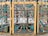 Intricately designed wrought iron gate with vivid colors and ornate patterns, featuring a series of stylized animals, floral motifs, and scrollwork. The dominant colors are teal, yellow, and red, with the gate framed by gilded panels accentuated with detailed blossoms and curlicues.