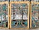 Intricately designed wrought iron gate with vivid colors and ornate patterns, featuring a series of stylized animals, floral motifs, and scrollwork. The dominant colors are teal, yellow, and red, with the gate framed by gilded panels accentuated with detailed blossoms and curlicues.