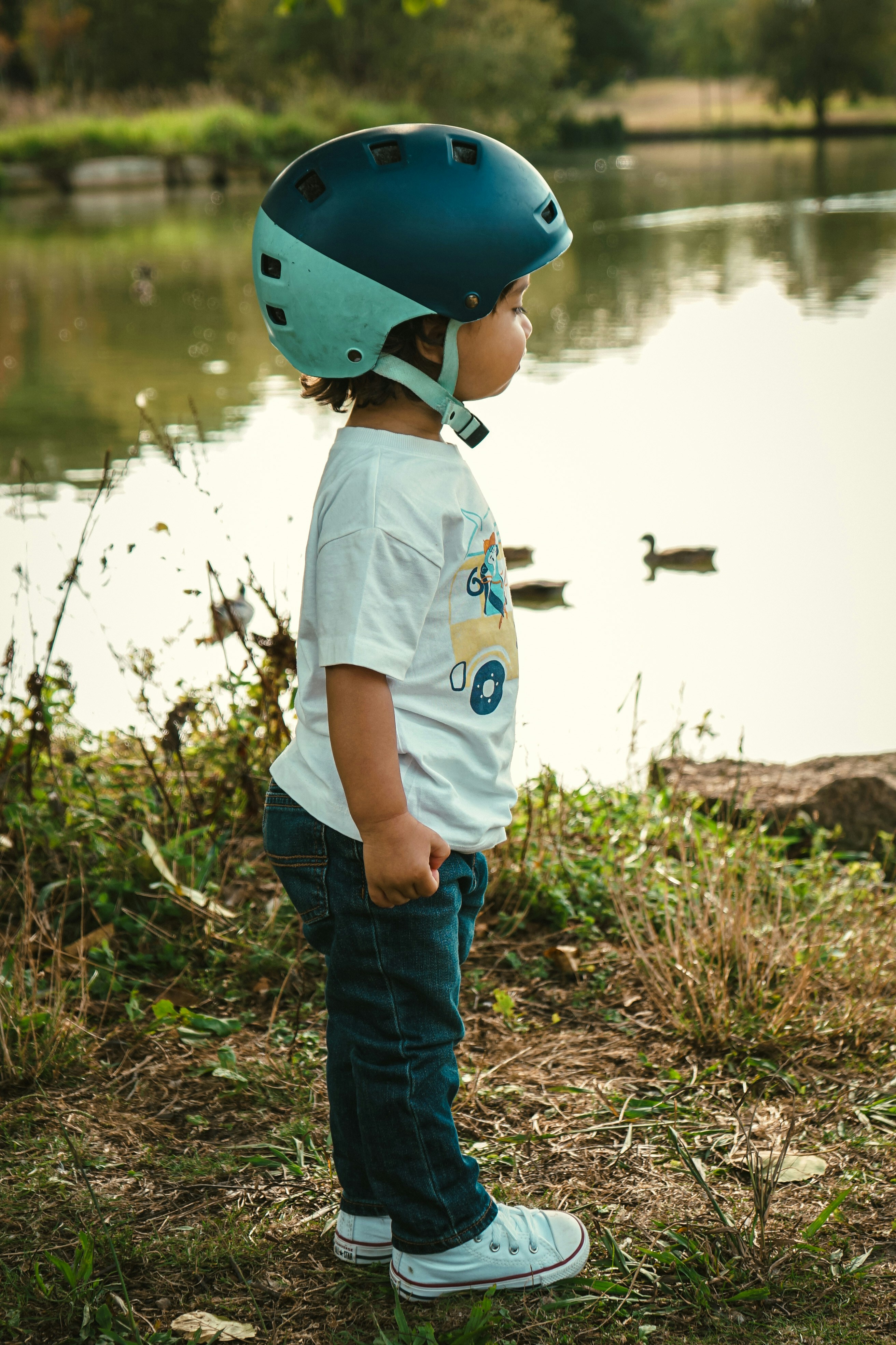 a young boy wearing a helmet standing next to a lake