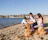 A happy family enjoying a sunny day on the beach with their dog playing nearby.