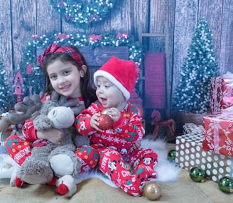 two little girls sitting next to a christmas tree