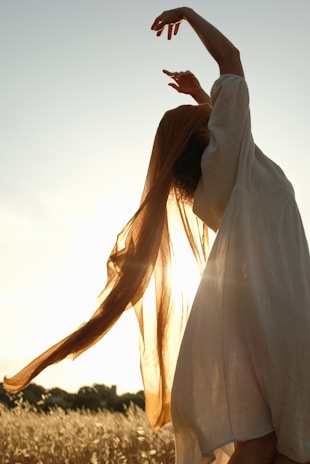 A graceful female model dressed in a flowing rose gold silk dress in warm natural light.