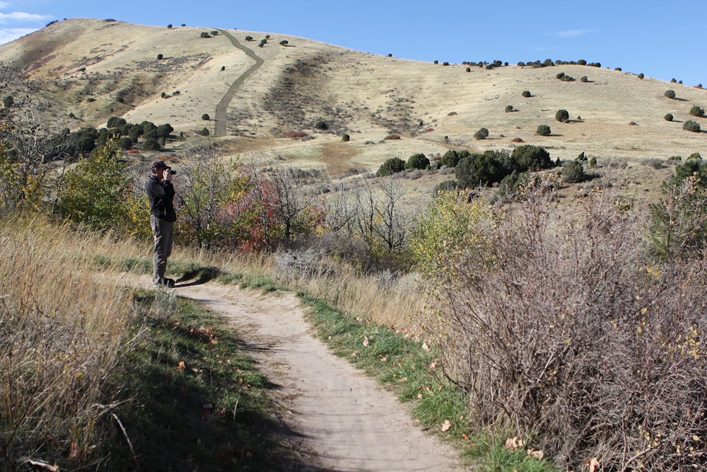 a man standing on a dirt road in the middle of a field