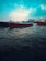 Several boats with red hulls are floating on a vast body of water under a partly cloudy sky. The water has gentle ripples, and the sky is a bright blue with some white clouds.