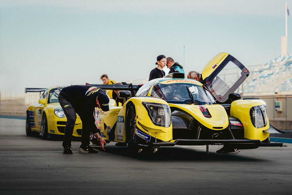 a group of people standing around a yellow race car