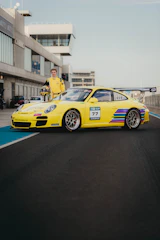 Hugo Becerra in racing gear standing beside a sleek racecar on a sunlit track.