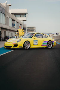 Hugo Becerra in racing gear standing beside a sleek race car on a sunlit track.