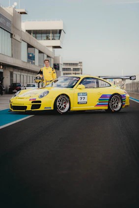 Hugo Becerra in racing gear standing beside a sleek racecar on a sunlit track.