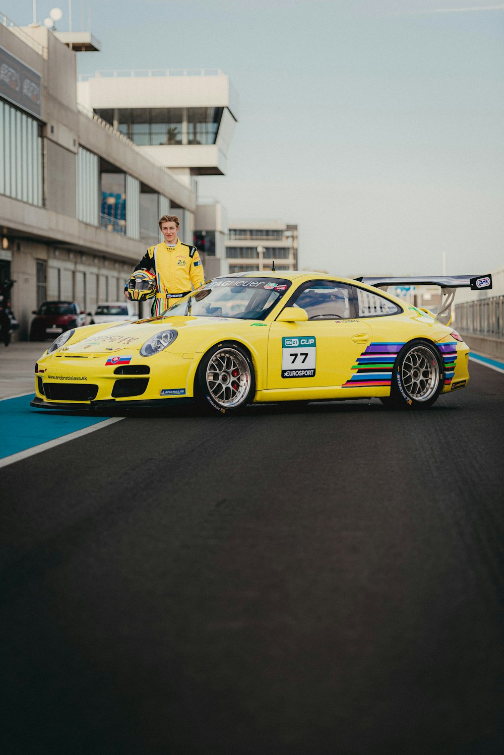 a man standing next to a yellow car on a race track