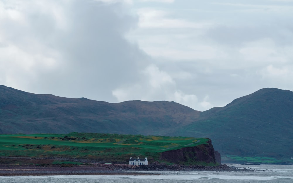 a house on the shore of a body of water with mountains in the background