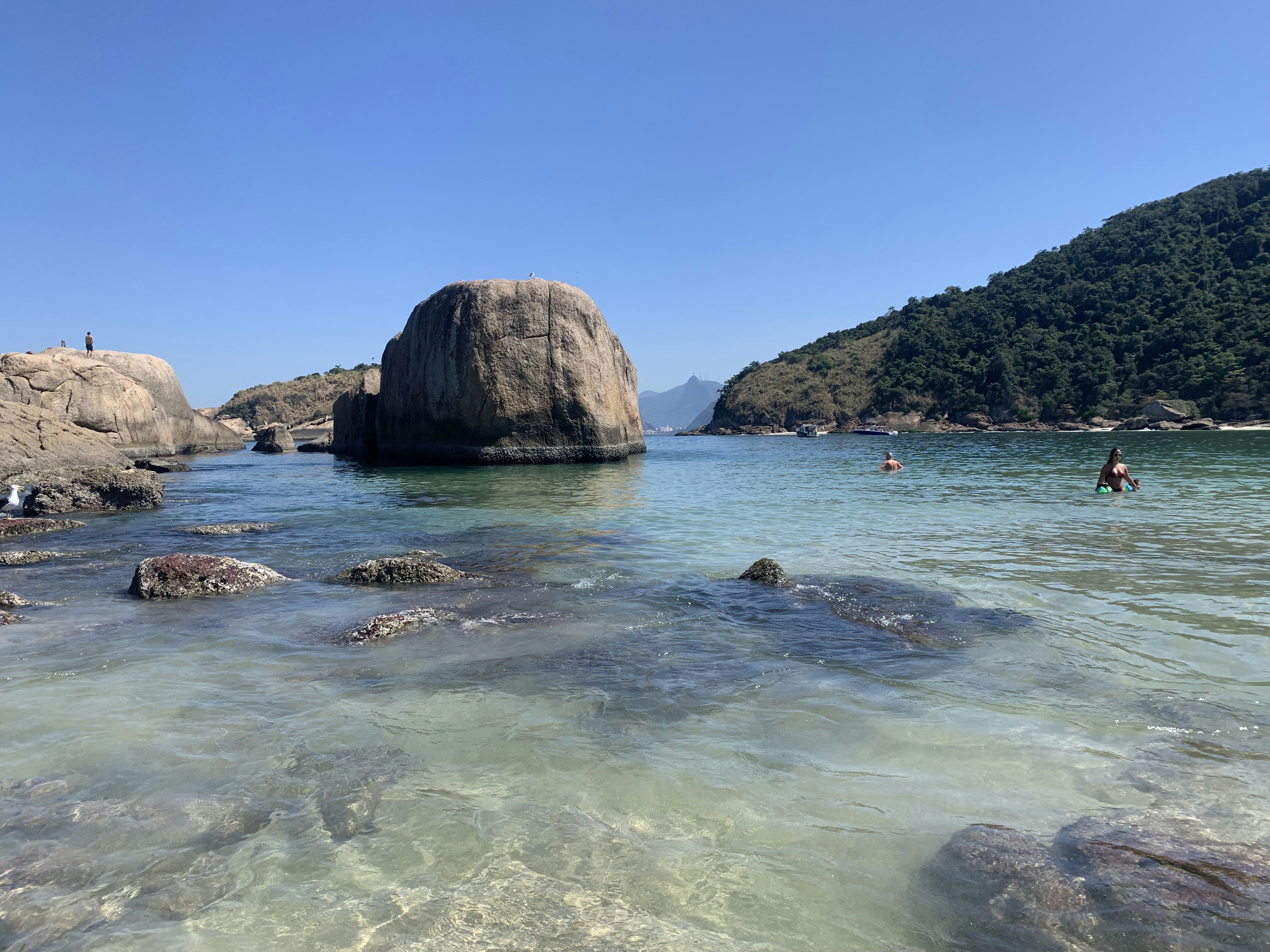 a person swimming in a body of water next to a large rock