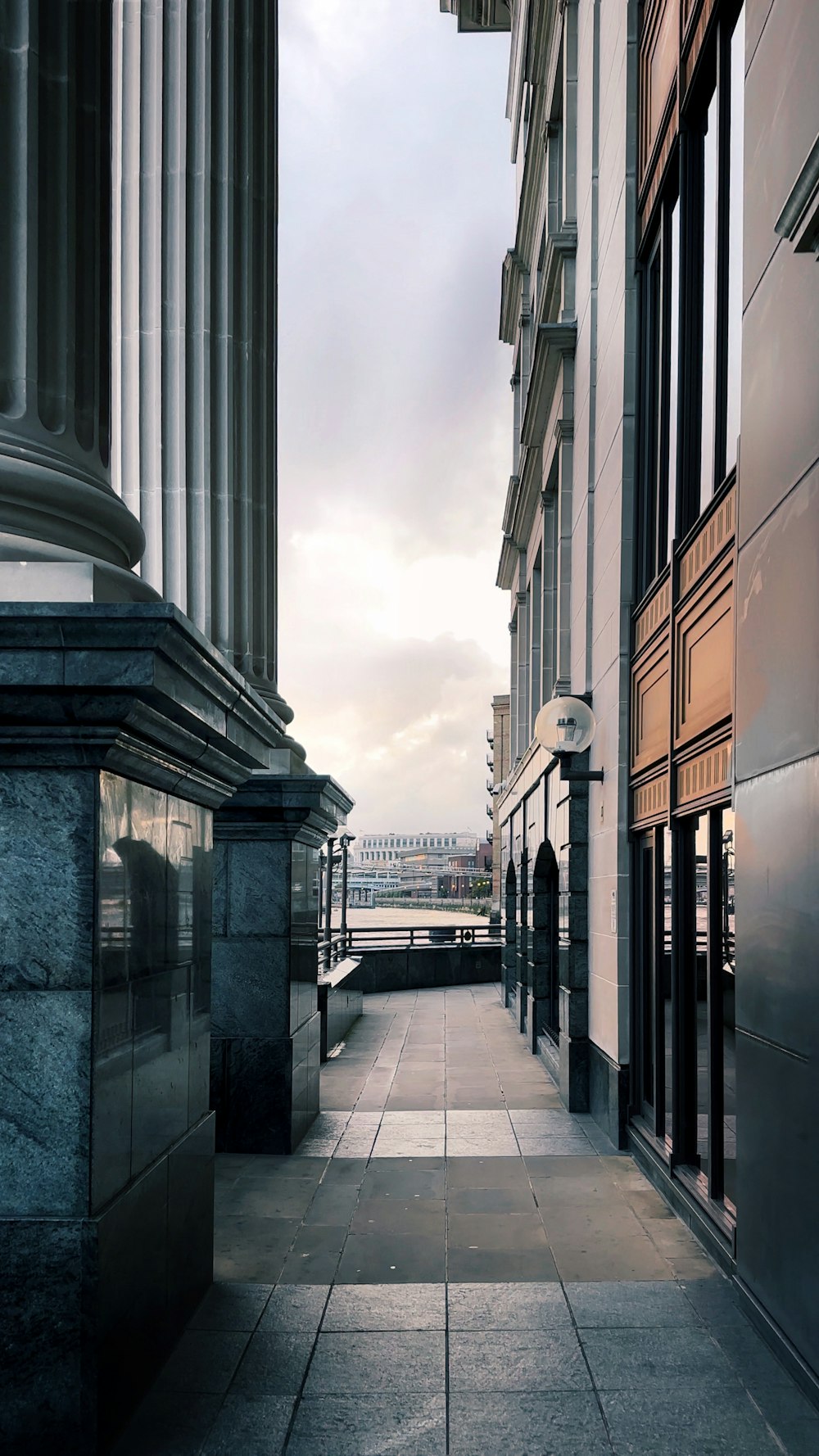 an empty sidewalk between two buildings on a cloudy day