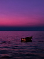 A small fishing boat gently rocking with colorful skies reflecting on the sea at dusk.