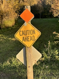 a caution sign on a wooden post in the grass
